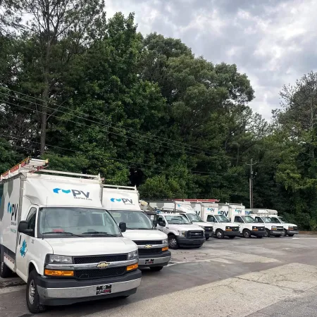 Fleet of white PV Heating and Air service vans parked in a row under a cloudy sky near trees.