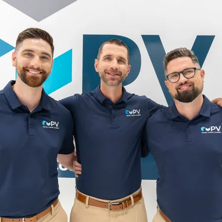 Three smiling men in navy polo shirts with PV logo standing in front of branded wall, arms around each other.