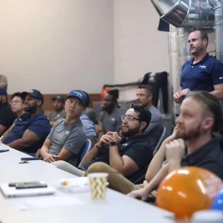 Team of professionals attending a meeting in a modern industrial office room with safety helmets on the table.