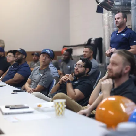 Team of professionals attending a meeting in a modern industrial office room with safety helmets on the table.