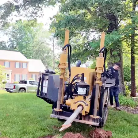 Horizontal directional drilling machine digging underground near residential house with worker and green trees