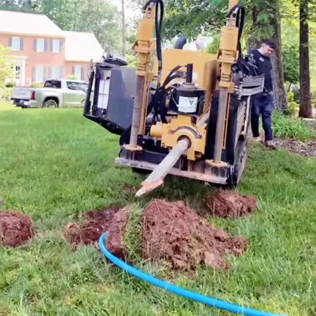 Horizontal directional drilling machine digging underground near residential house with worker and green trees