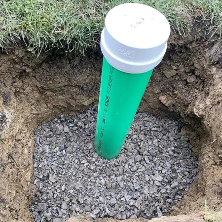 Green PVC pipe with white cap installed in gravel-filled hole surrounded by grass in yard