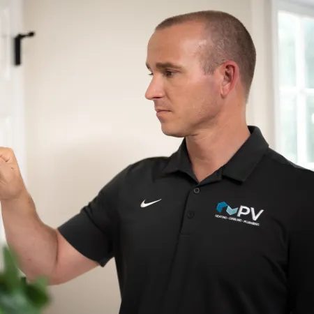 Technician in black PV Heating shirt adjusting a thermostat on a white wall in a residential setting
