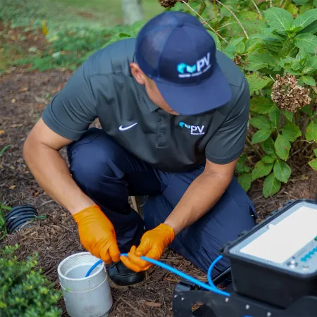 Technician in uniform kneeling outdoors connecting blue fiber optic cables to testing equipment.