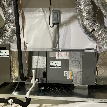 Central HVAC unit with ducts, piping, and electrical connections installed in an insulated attic space.