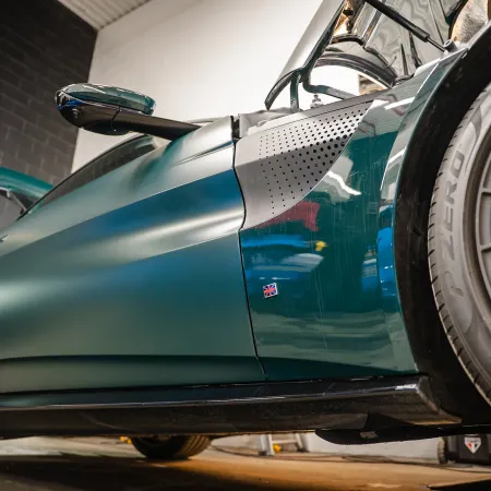 Close-up of a sleek green sports car side with red brake calipers and detailed aerodynamic design.