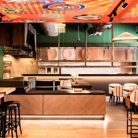 Modern restaurant interior with wooden tables, striped chairs, green walls, and artistic ceiling decorations