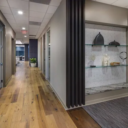 Modern office hallway with wooden floor, glass doors, decorative wall niche with sculptures and books.