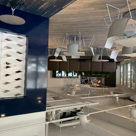 Modern office lounge with white chairs, brown couches, abstract wall art, and large windows with blinds.