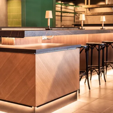 Modern wooden bar counter with stools and warm ambient lighting in a contemporary restaurant interior.