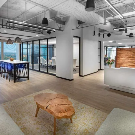 Modern office space with natural wood accents, open seating, glass conference room, and city views through large windows.