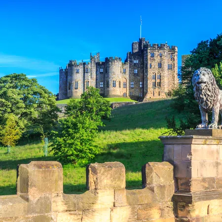 Historic stone castle on a hill with lush greenery and a lion statue on a stone pedestal in the foreground.