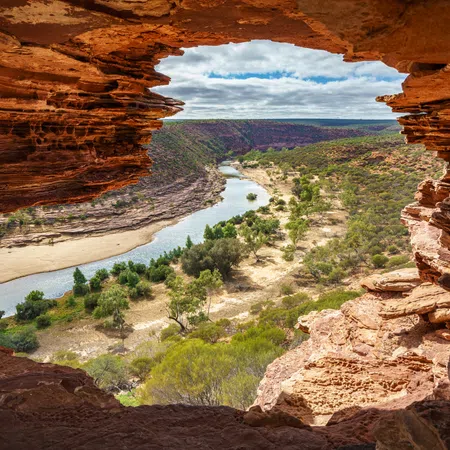 View of a winding river and green vegetation through a rocky cave opening under a cloudy sky.