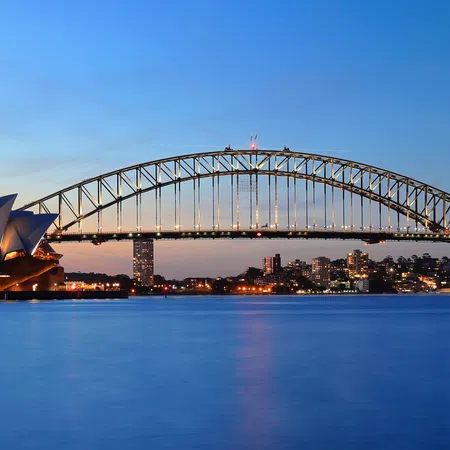 Sydney Opera House and Harbour Bridge at dusk with city skyline and calm water reflecting lights.