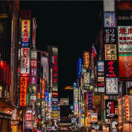 Night street scene in a Japanese city lit by numerous colorful neon and LED signs on buildings.