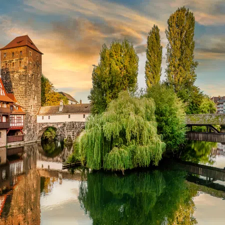 Historic stone bridge and timber-framed buildings reflected in calm river at sunset in scenic European town.