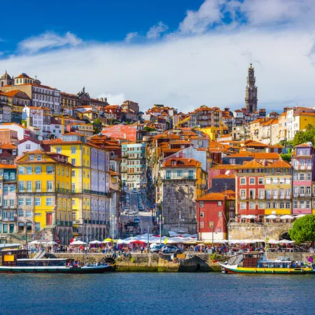 Colorful historic buildings along the Douro River in Porto, Portugal with boats and clear blue sky.