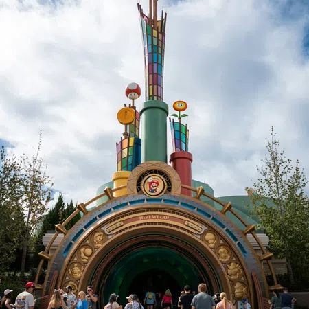Entrance to a colorful Mario-themed tunnel with families walking inside under a partly cloudy sky.