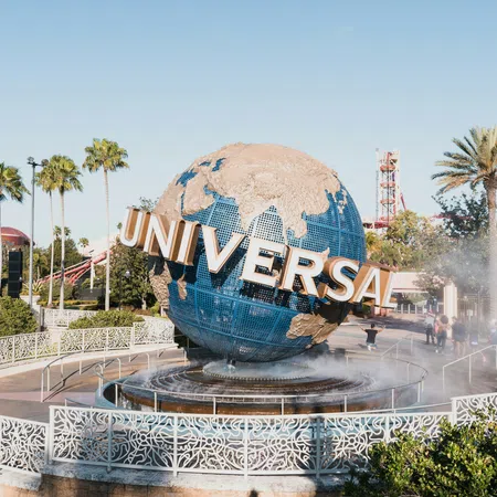 Universal Studios globe fountain surrounded by palm trees and clear skies at theme park entrance.