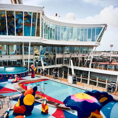 Colorful water playground with a pool, abstract sculptures, and modern cruise ship deck under a blue sky.