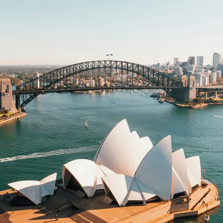Aerial view of Sydney Opera House and Harbour Bridge over blue water with city skyline in the background