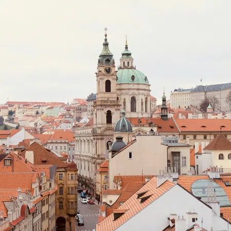 View of Prague city with red rooftops and historic St. Nicholas Church featuring green domes and clock tower.