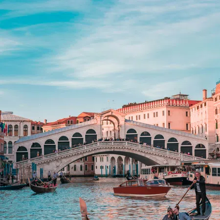 Gondola with tourists and Rialto Bridge over Grand Canal in Venice under blue sky at sunset.