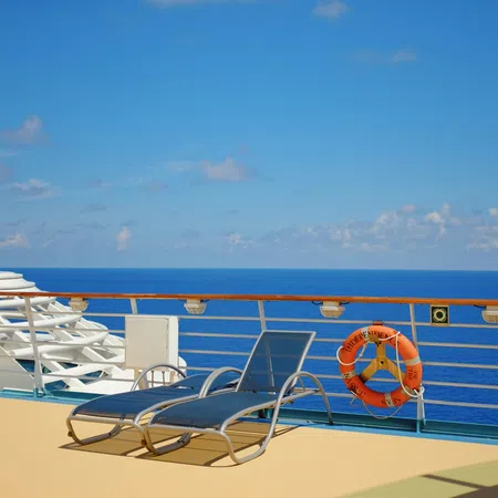 Two lounge chairs on a cruise ship deck overlooking calm blue ocean under a partly cloudy sky
