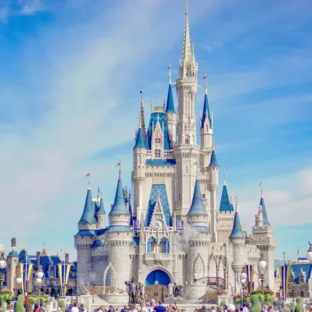 Daytime view of Cinderella Castle with blue turrets and clear sky at a theme park with visitors.