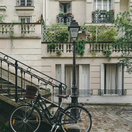 Black bicycle parked by a vintage street lamp next to stairs outside a classic Parisian building with balconies and greenery.