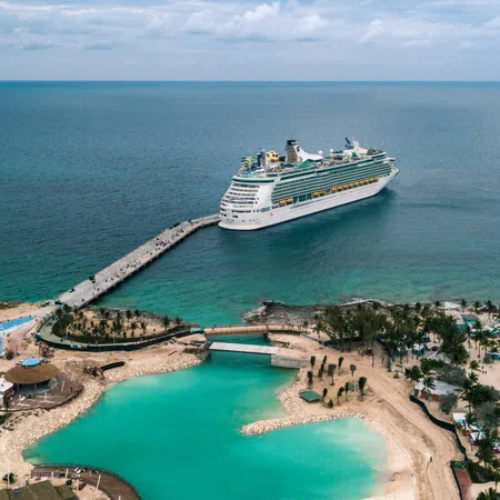 Large cruise ship docked near tropical island resort with turquoise lagoon and sandy beaches under cloudy sky