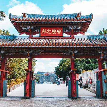 Traditional red and blue Japanese torii gate with tiled roof surrounded by greenery and visitors walking through.