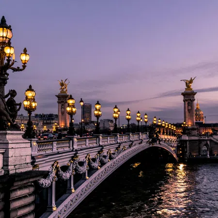 View of the illuminated Alexandre III Bridge over the Seine River in Paris during twilight with classical lamp posts.