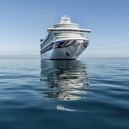 Large cruise ship with a Union Jack design on the bow reflecting on calm ocean waters under a clear sky.
