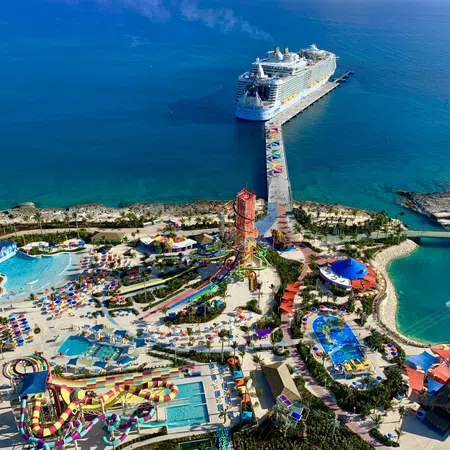 Aerial view of tropical water park with slides, pools, colorful umbrellas, and cruise ship docked at pier
