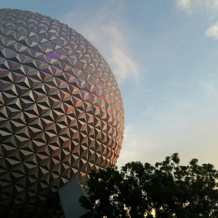 Epcot's iconic geodesic sphere at sunset with sky and silhouetted trees in the foreground.