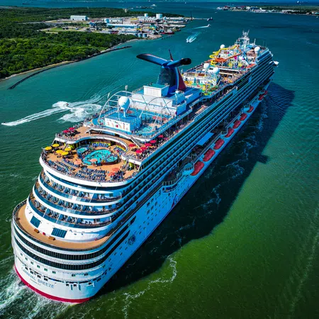 A large cruise ship sails through a river with passengers on deck enjoying pools and water slides on a sunny day.