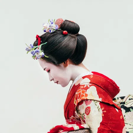 Japanese woman in traditional red kimono with floral patterns and elaborate hair accessories bowing gracefully.
