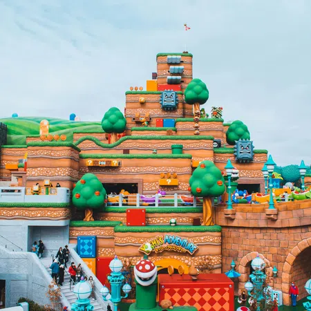 Colorful Super Mario-themed amusement park with iconic gaming elements and visitors exploring the area under a cloudy sky