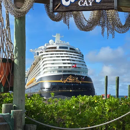 Disney Castaway Cay sign with cruise ship docked and lush greenery under sunny blue sky.