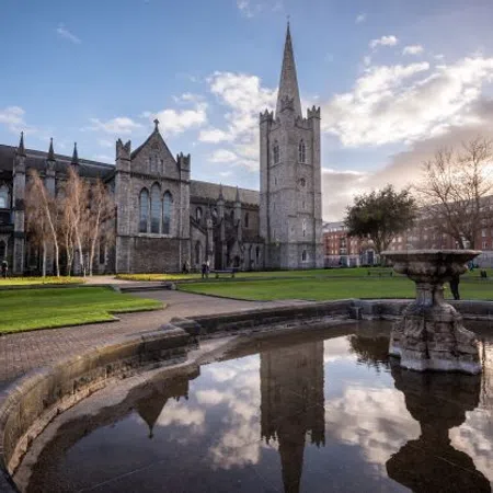 Historic St Patrick's Cathedral in Dublin reflected in a fountain pool with clear sky and park surroundings