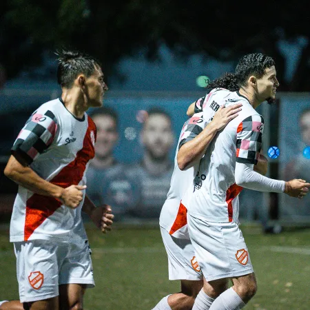Soccer players in white and red uniforms celebrating on the field during a nighttime match.