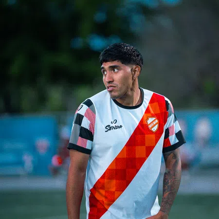 Young male soccer player in a white and red jersey standing on the field looking to his left.