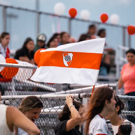Fans waving a white and orange flag with a sports emblem at a stadium event filled with spectators.
