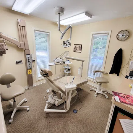 Dental office with dental chair, x-ray machine, stools, and equipment in a well-lit room.