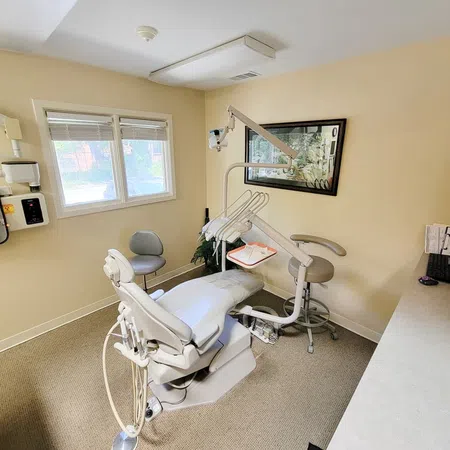 Bright dental clinic room with chair, dental equipment, and computer on countertop under window.
