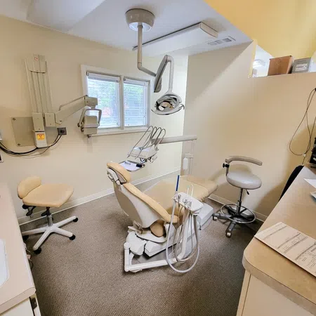 Bright dental office with beige dental chair, equipment, computer, and clock on wall under window
