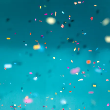 Colorful confetti pieces scattered and falling against a bright teal background, creating a festive atmosphere.