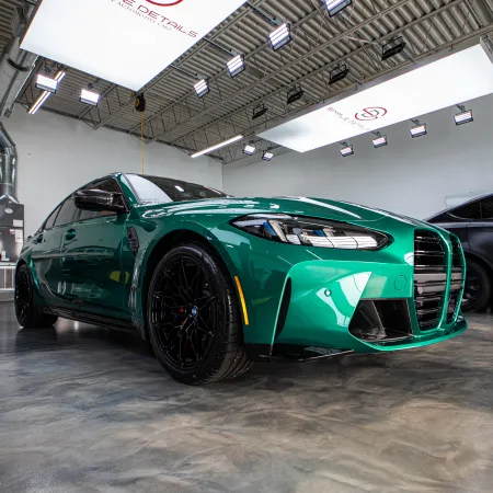 Green sports sedan with black rims parked in a bright, modern detailing garage with another black car nearby